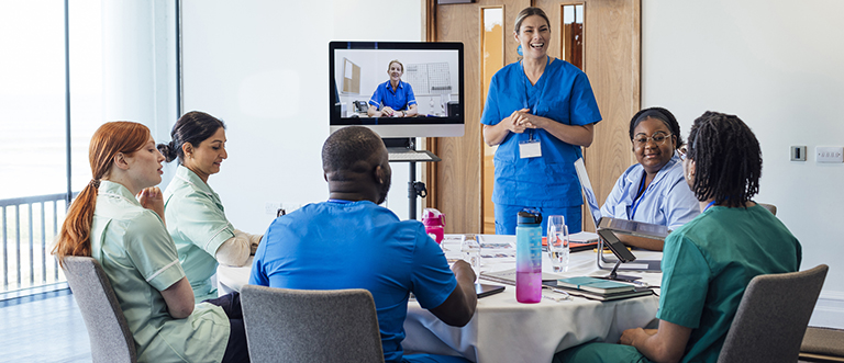 Efficiency and Excellence A group of healthcare professionals sitting around a table, taking part in a medical training meeting in a medical building in Whitley Bay, North East England. They are all listening to a webinar on a computer that a nurse is hosting while they listen to another healthcare professional talking to the whole group as she stands next to the screen.
Videos available for this scenario.