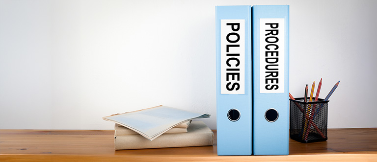 Folders labelled “Policies” and “Procedures” on a desk, representing organised document management in healthcare settings.